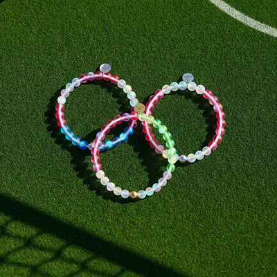 NOGU 2026 Nations Bracelets with translucent multicolor beaded designs displayed on a green soccer field.