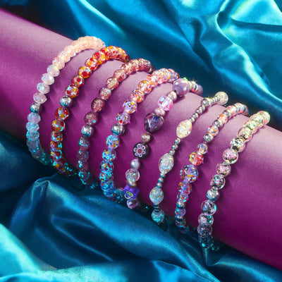 NOGU Jewel Tones collection stack of colorful gemstone-inspired beaded bracelets on purple fabric with turquoise satin.