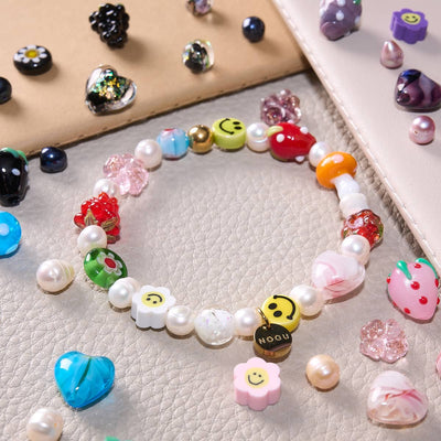 NOGU Beautiful Chaos gold-tone bracelet with pearl beads, colorful glass charms, smiley flowers, cherries and strawberry accents.