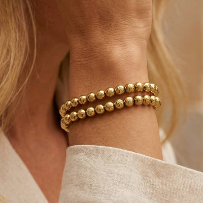 Gold-tone Essential Hardware bracelet with engraved 5mm round beads, styled in a layered stack on a wrist.