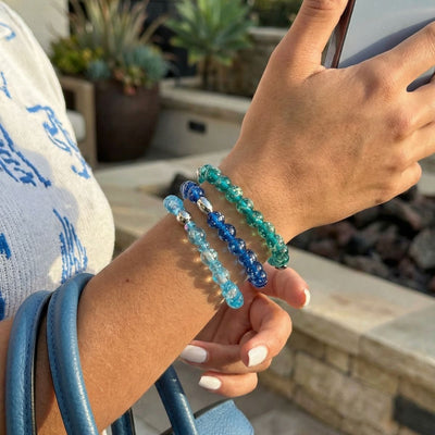 NOGU Made to Pair Aquamarine Ice Snow Globe bracelet layered with luminous aqua, blue and teal beaded bracelets.