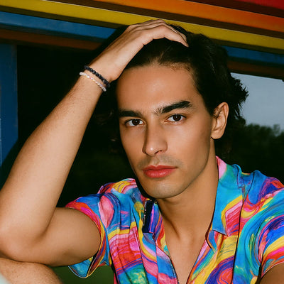 NOGU NO BOXES collection model wears stacked black and pastel beaded bracelets with a colorful patterned shirt.