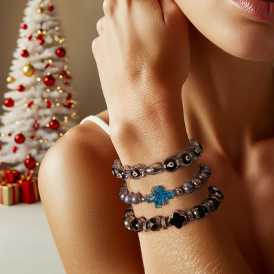 NOGU Meaningful Gifts stack of gray beaded bracelets with black flower and blue crystal accents, styled for holiday giving.