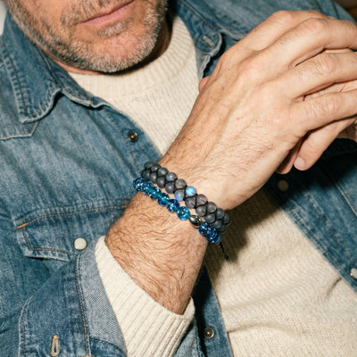NOGU Gifts for Him collection features a man wearing layered blue and black beaded bracelets with denim.