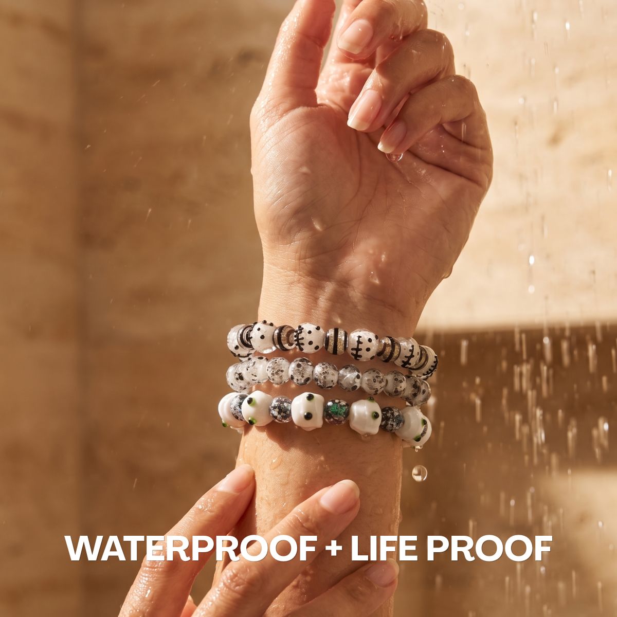 Stacked white and black beaded bracelets with silver accents worn on a wrist under running water.