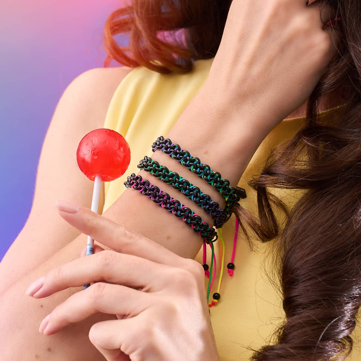 Macaw Links Mini Kismet Bracelets in rainbow spectrum with gunmetal links on adjustable cords worn on wrist holding red lollipop by NOGU