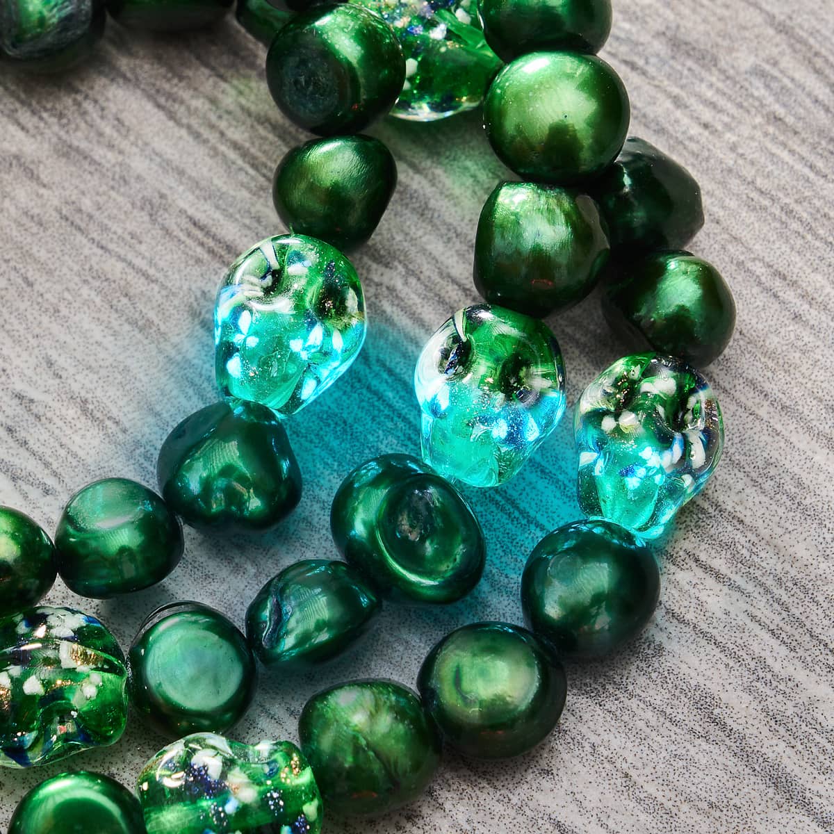 Emerald Crown bracelet close-up of green freshwater pearl beads and glowing firefly glass skull beads on a textured surface by NOGU