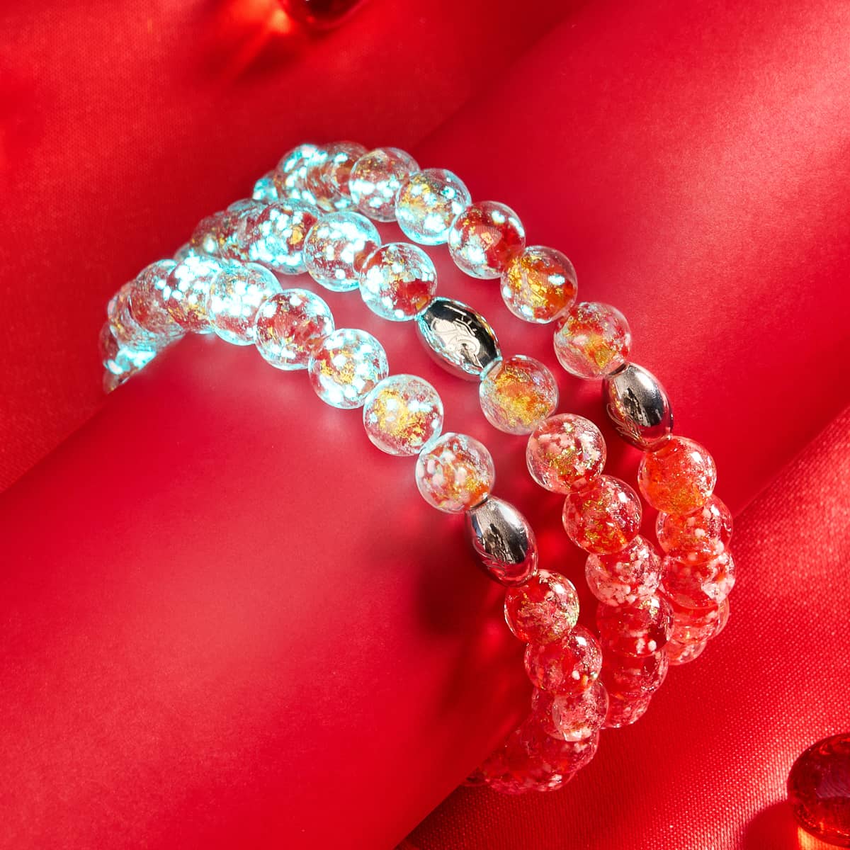 In Love Firework Glass bracelets with luminous blue and red beads, silver clasps on red fabric background by NOGU