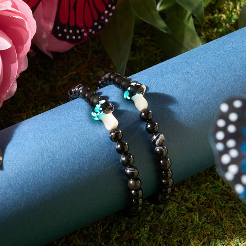 Black Agate bracelets with glowing Firefly Glass mushroom beads displayed on blue cylinder with moss and flowers background by NOGU