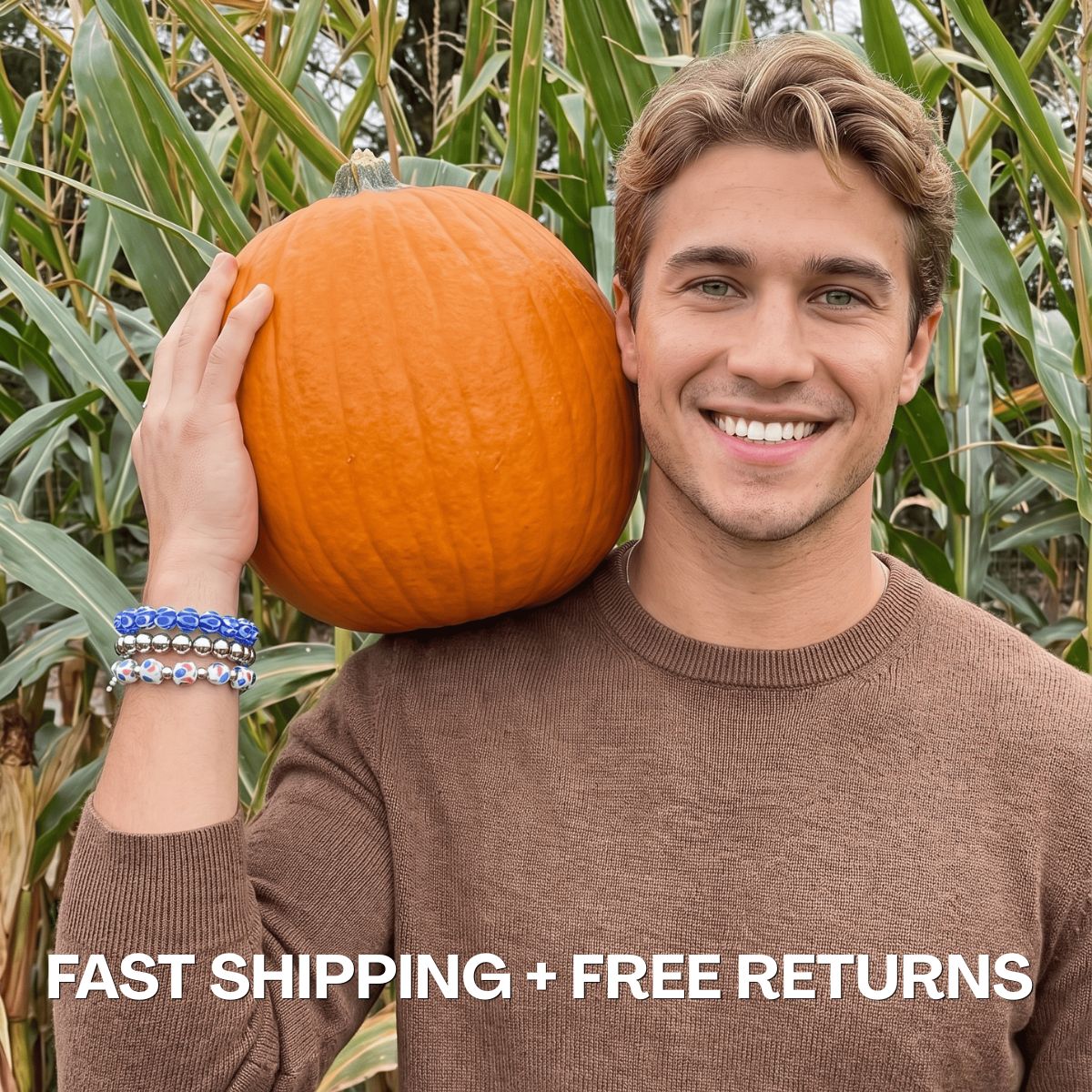Model wearing stacked blue and multicolor beaded bracelets while holding an orange pumpkin in a cornfield.