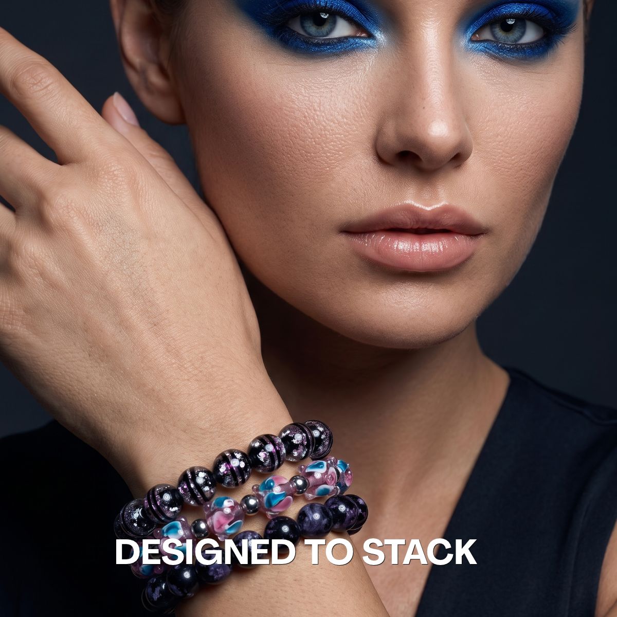 Model wears a stack of NOGU beaded bracelets with black, purple, pink and turquoise glass beads and silver-tone accents.
