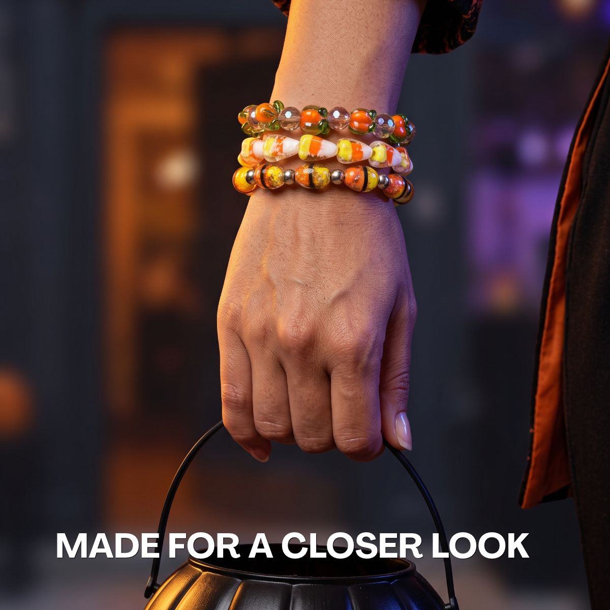 Stacked beaded bracelets in orange, green, white and gold tones worn on a wrist, styled with a black handbag.