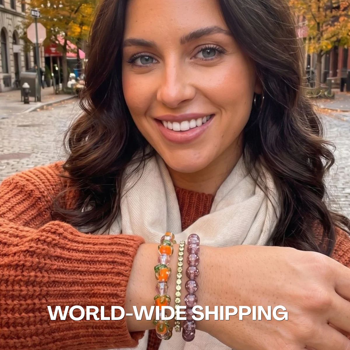 Woman wearing stacked beaded bracelets with orange, green, lavender and gold-toned beads, styled with an autumn knit sweater.