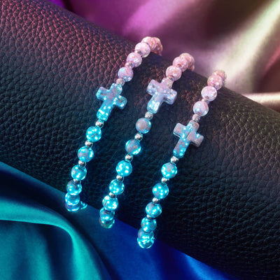 Periwinkle Firefly Glass Cross Bracelets with glowing glass beads and stainless steel accents displayed on black textured surface by NOGU