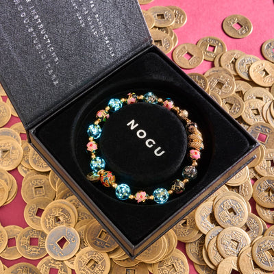 Shadow Dragon bracelet with glowing Onyx Firefly glass, enamel lotus beads, and gold-plated serpent charm in black NOGU box on ancient coins