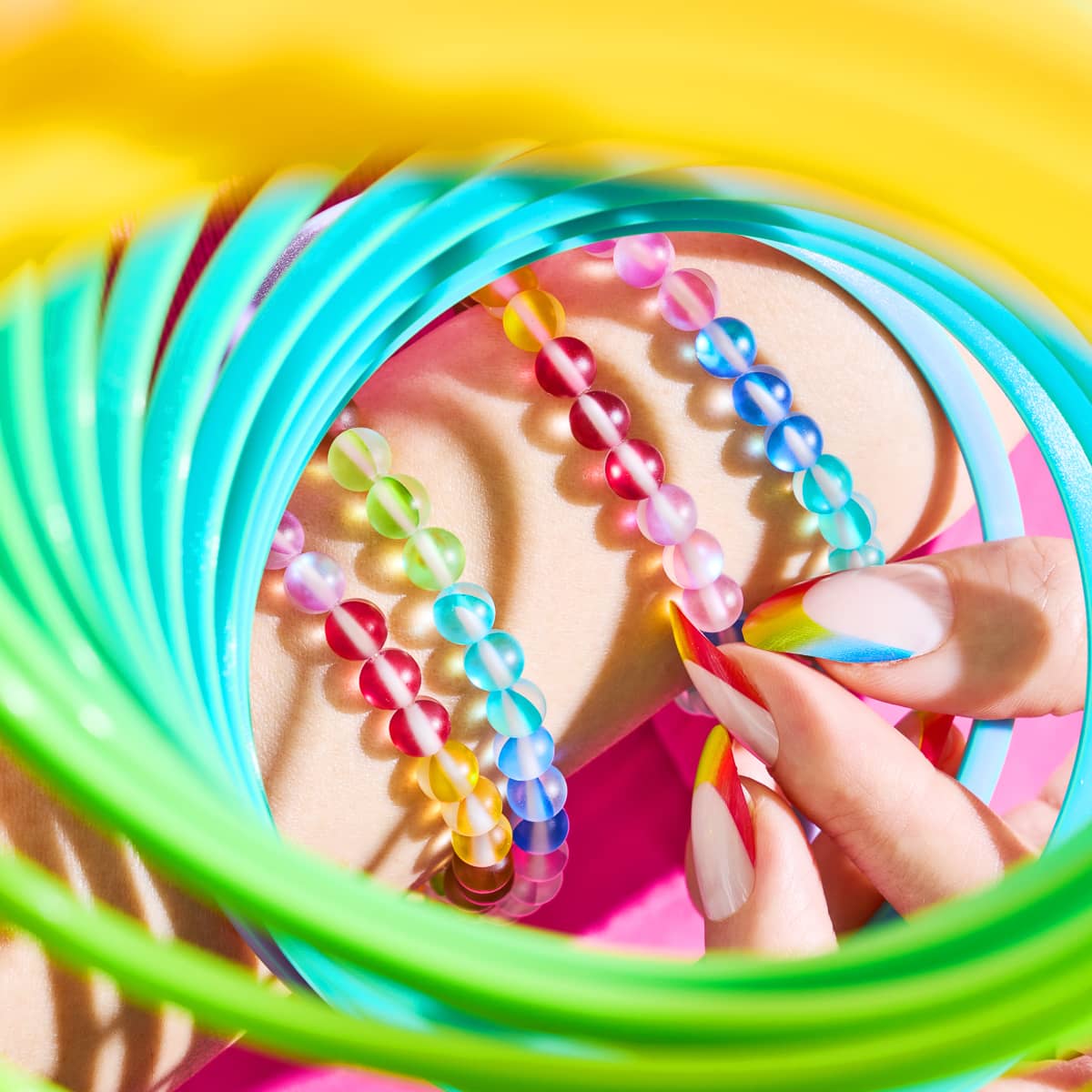 Rainbow Wrap Mermaid Glass Bracelet with translucent multicolored beads worn on wrist surrounded by colorful plastic rings by NOGU