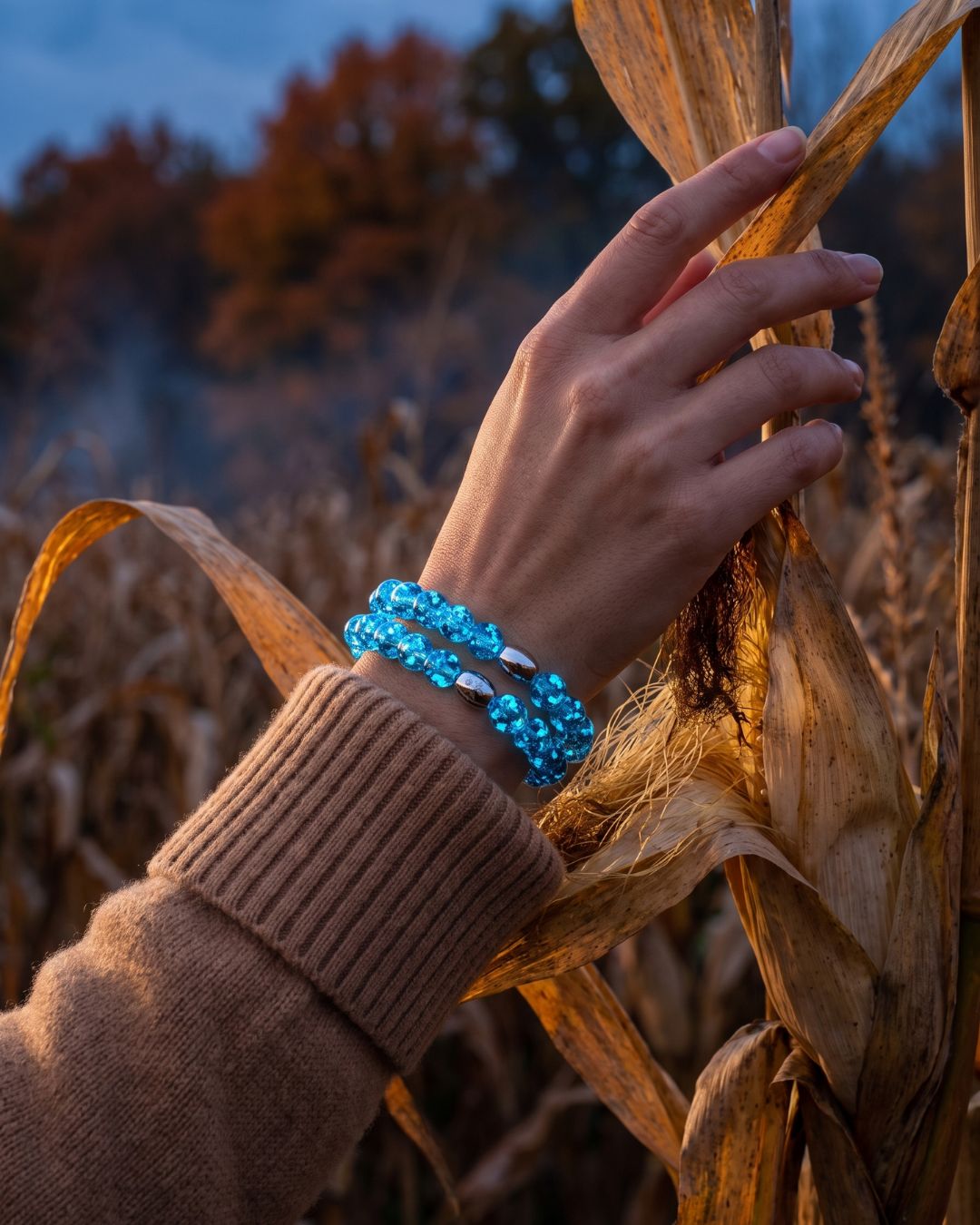 Stacked bright blue beaded stretch bracelets with polished silver-tone oval accents, worn in a golden cornfield.