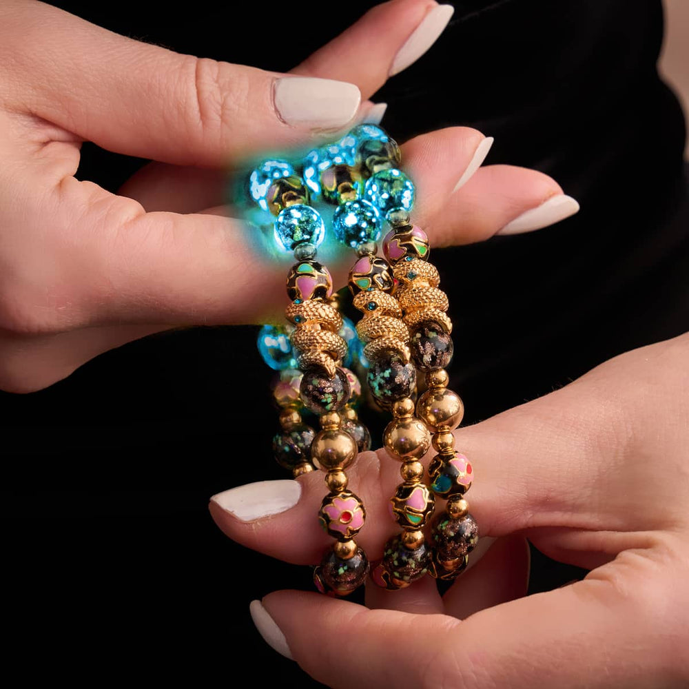 Shadow Dragon bracelets with glowing onyx Firefly glass beads, enamel lotus beads, and 18k gold-plated serpent charms held in hands by NOGU