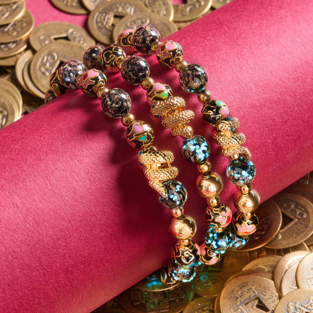 Shadow Dragon bracelet with glowing onyx Firefly glass and enamel lotus beads with 18k gold-plated serpent charm on red cushion by NOGU