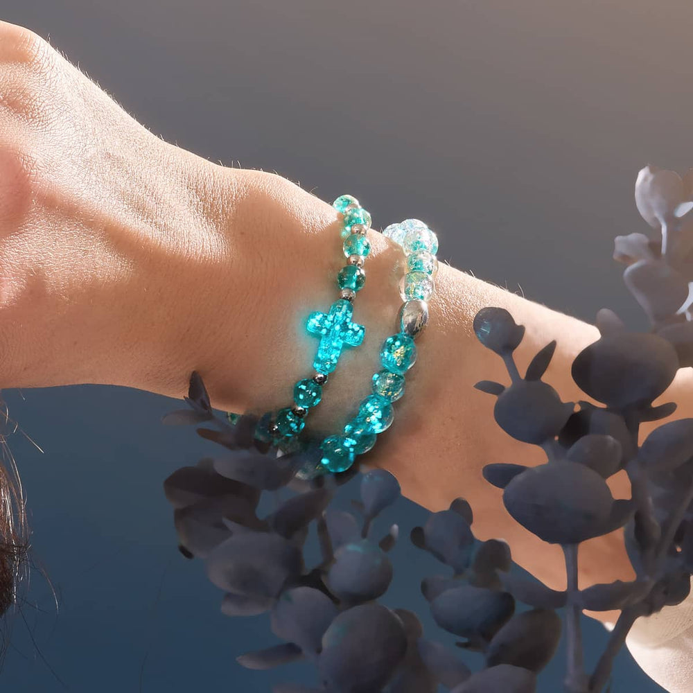 Aurora Spark bracelet with turquoise and gold flecked Firework Glass beads and stretch cord next to blue glass cross bracelet by NOGU