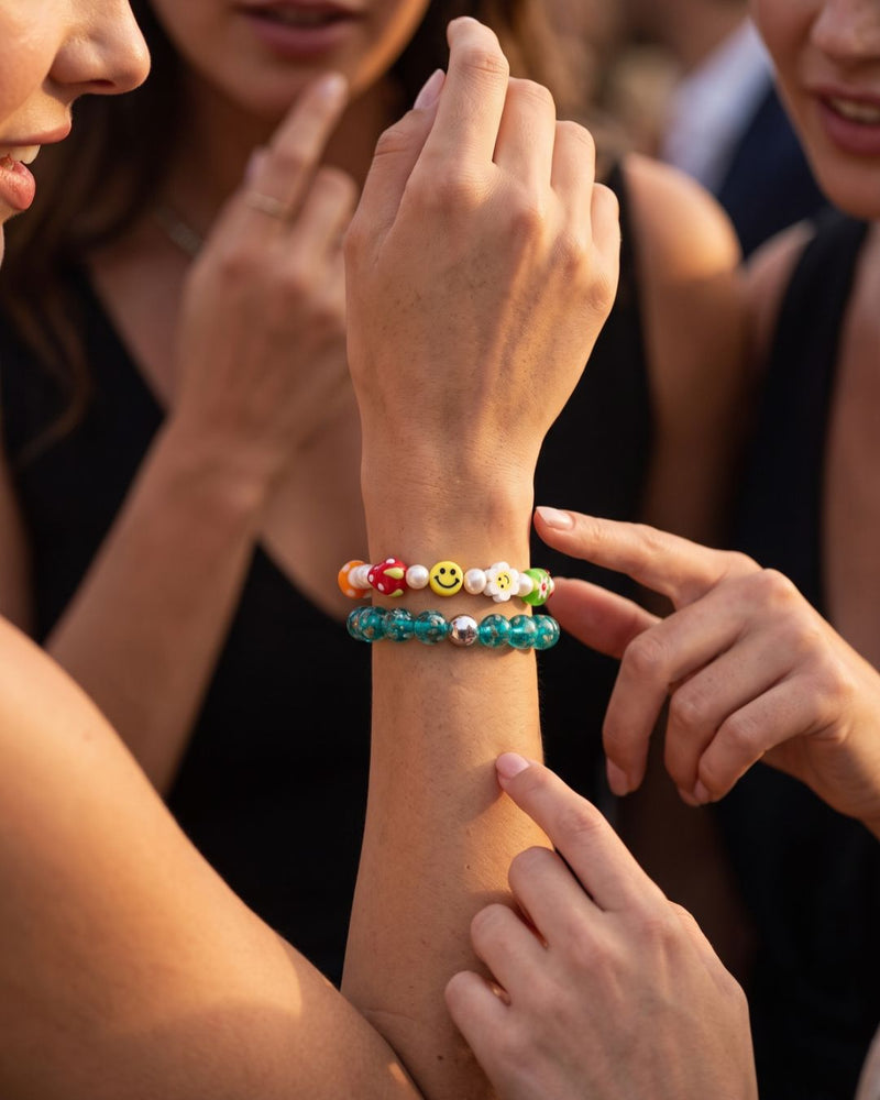 Stacked beaded bracelets with turquoise glass beads and colorful smiley, mushroom and flower charms on a wrist.